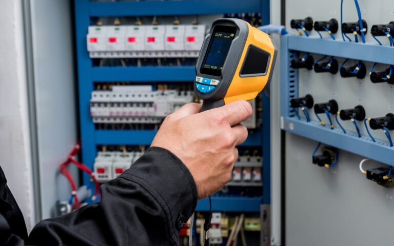Hand holding a thermal imaging camera inspecting an electrical panel.
